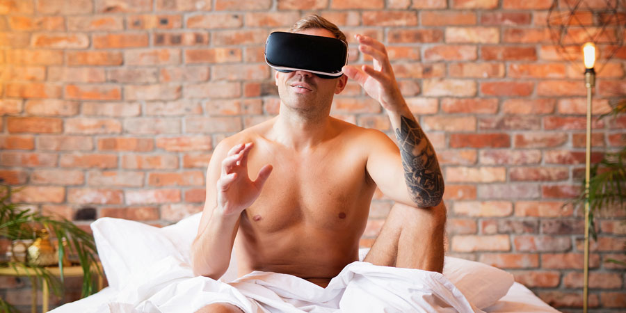 Attractive bare chested young man sitting in bed with a virtual reality headset using AI