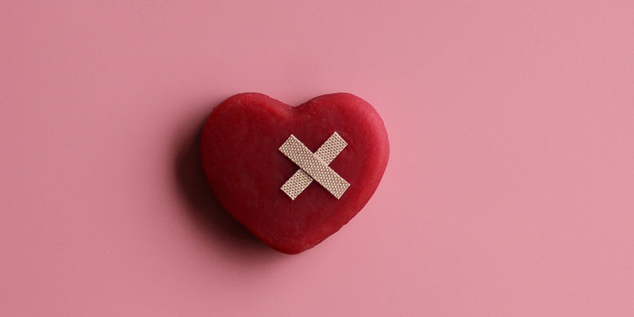 Red toy heart with bandaids to indicate that it is broken hearted but being healed