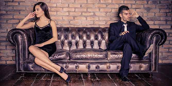 Woman and man sitting at opposite ends of a Chesterfield lounge in a swingers club