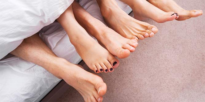 Three pairs of feet sticking out from under a doona during a threesome