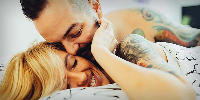 Young couple with tattoo sleeves cuddling in bed after having casual sex
