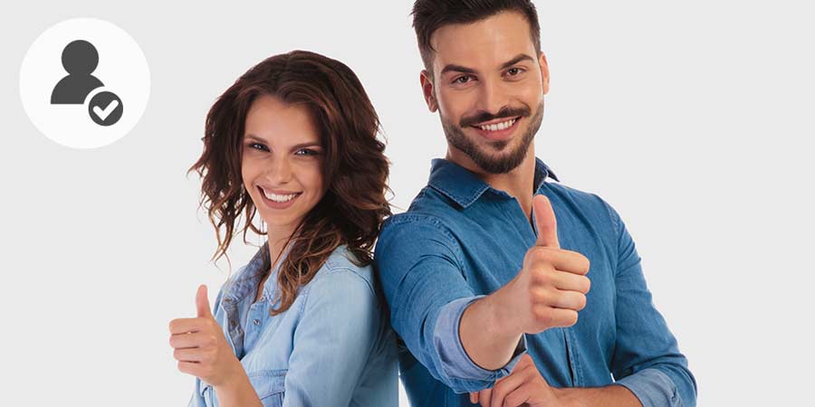 Smiling couple standing back to back giving thumbs up sign