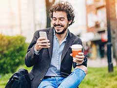 Handsome man reading a message on his mobile device while drinking a coffee