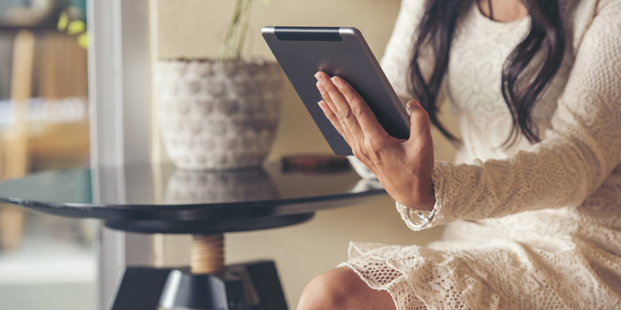 Woman wearing a cream lace dress sitting at a table checking her online messages