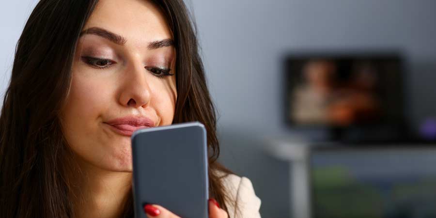 Attractive brunette woman pulling a duck face whilst reading a message on her mobile device