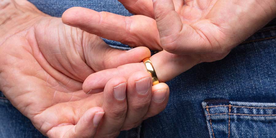 Close up of a man's hands held behind his back as he removes his wedding ring