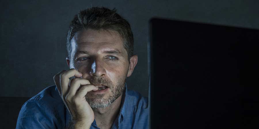 Man sitting in the dark staring at his computer screen watching porn