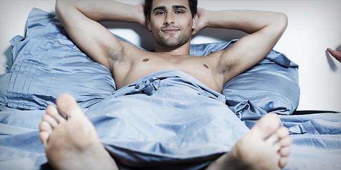 Handsome young man lying in bed with his hands behind his head looking satisfied