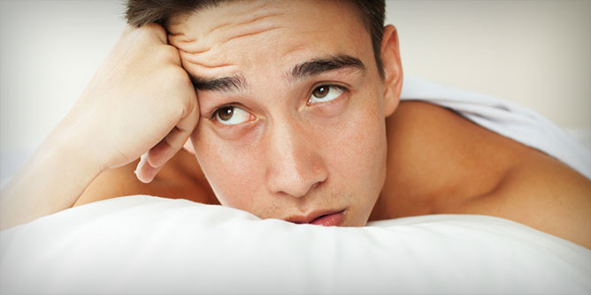 Young man lying in bed looking mournful because he's been rejected