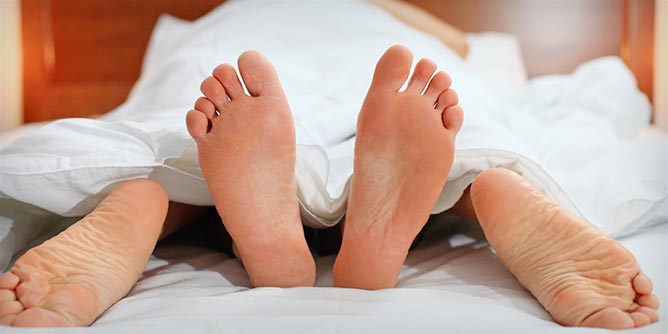 The feet of a swinger couple peeking out from under the doona