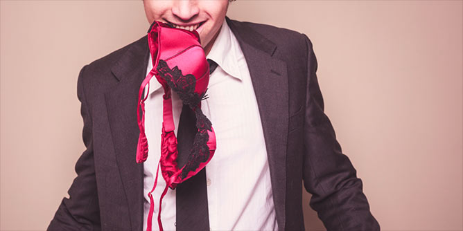 Man in a suit with a woman's red bra held between his teeth