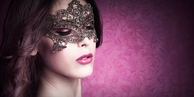 Beautiful woman wearing an intricate carnival mask in front of a background of pink flocked wallpaper