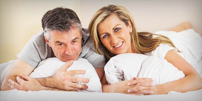 Mature couple lying together in bed looking at the camera