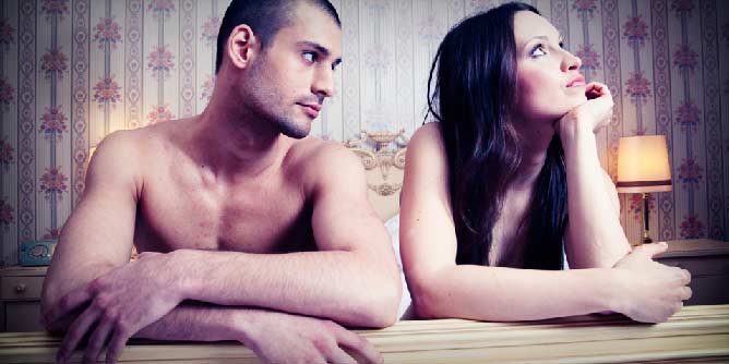 Couple lying in bed looking like the woman is upset because the man has made a mistake