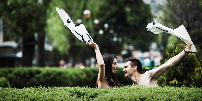 Couple throwing their clothes into the air ready to have public sex in a park