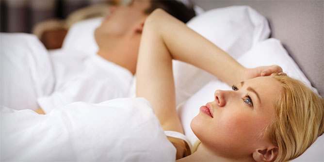Woman lying beside her partner in bed looking sad