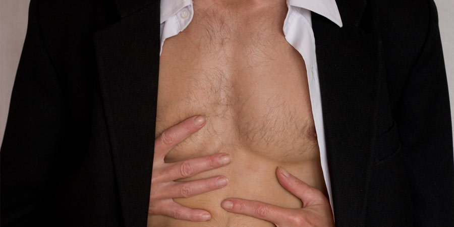 Torso of a man with his shirt and jacket unbuttoned and a woman's hands caressing his chest