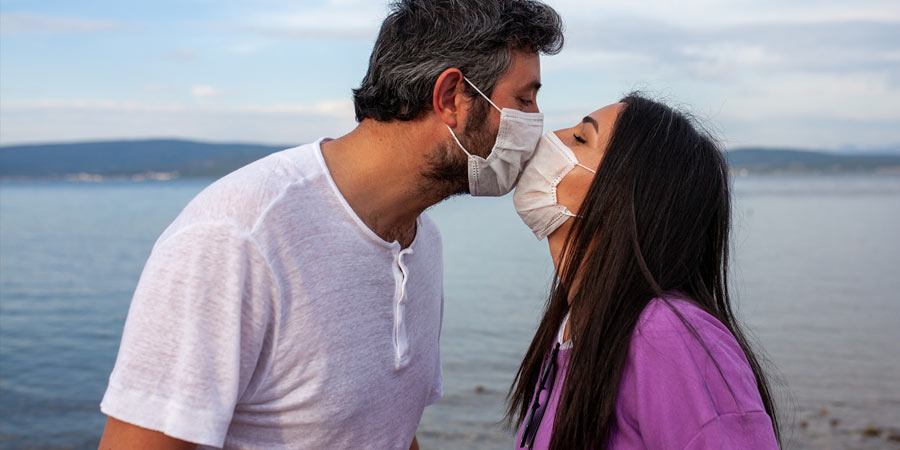Woman and man wearing masks due to covid19 sharing a kiss