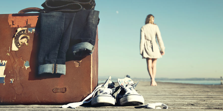 Woman walking away from an old battered suitcase sitting on a pier