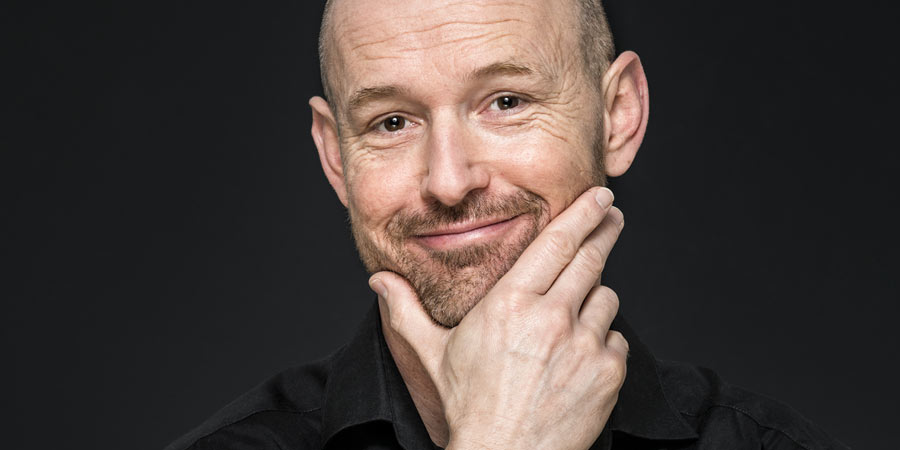 Mature man wearing a black collared shirt looking thoughtful 