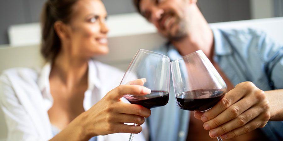 Couple sitting on a bedroom floor, partially nude, clinking glasses of red wine