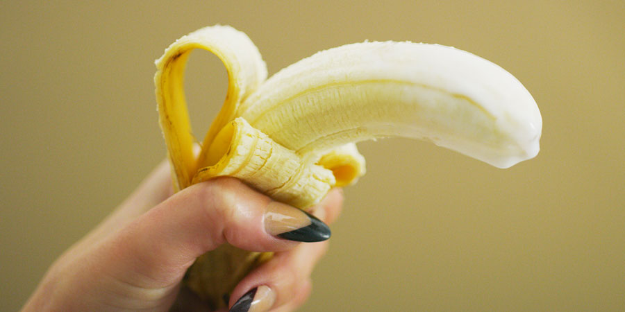 A woman holding a partly peeled banana to represent a woman giving a man a blow job
