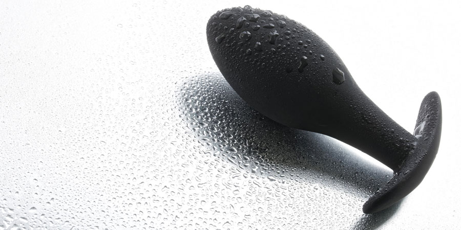Black butt plug resting on a white background with water droplets