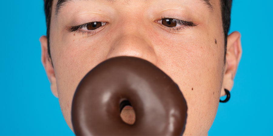 Close up of a man's face as he is about to lick a chocolate iced donut