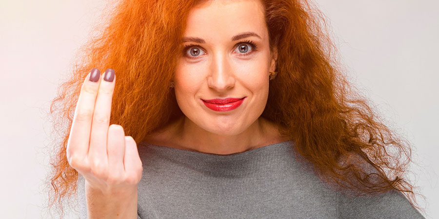 Woman with curly red hair smiling and holding up two fingers