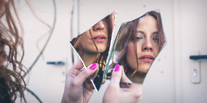 Woman looking at her reflection in a broken mirror