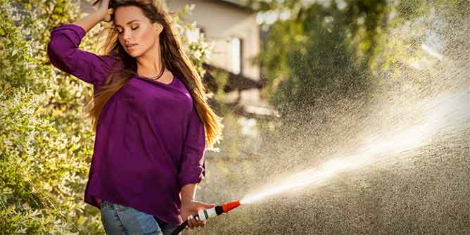 Woman holding a garden hose and spraying water to imply she is squirting