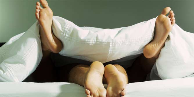 Two pairs of feet sticking out from under a doona cover