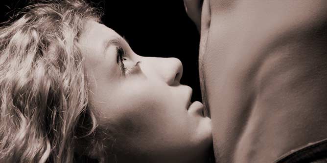 Woman kneeling in front of a man and looking up into his eyes seductively