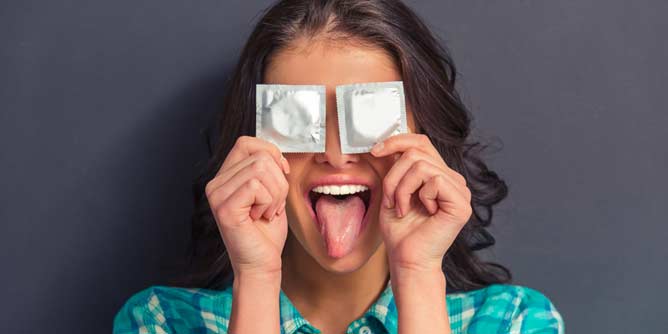 Woman holding up two condom packets over her eyes and pulling a face