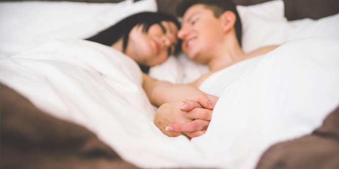 Woman and man in bed holding hands and smiling at each other