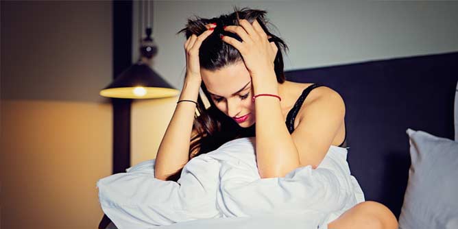 Woman sitting in bed looking frustrated with her head in her hands