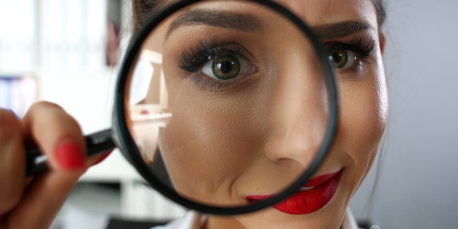 Woman looking through a magnifying glass appearing to inspect the camera