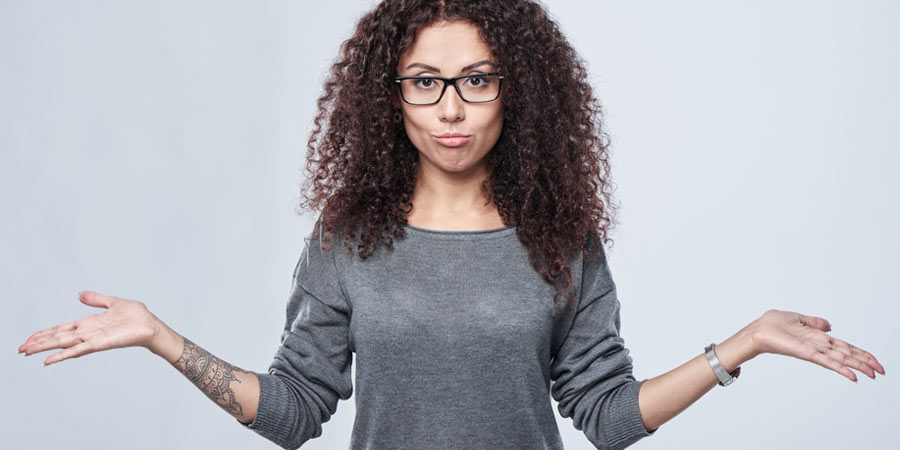 Attractive woman with tattoo, curly hair and glasses shrugging her shoulders