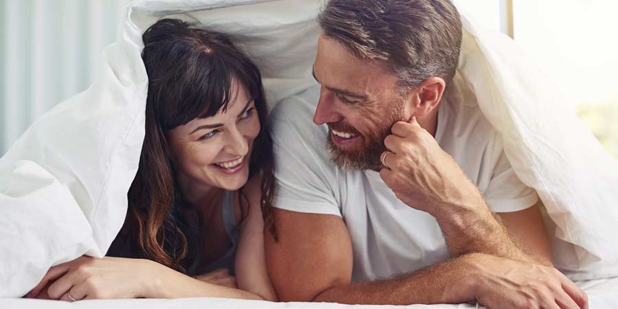 Man and woman snuggled under a doona smiling at each other