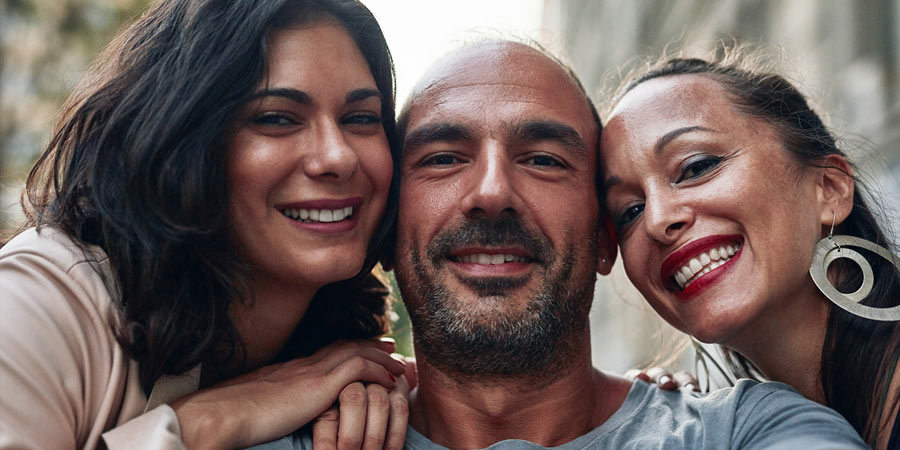 Man with his two female polyamorous partners smiling at the camera