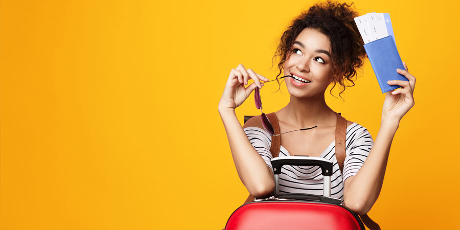 Woman holding plane tickets leaning on a red suitcase as she thinks about what she's packed