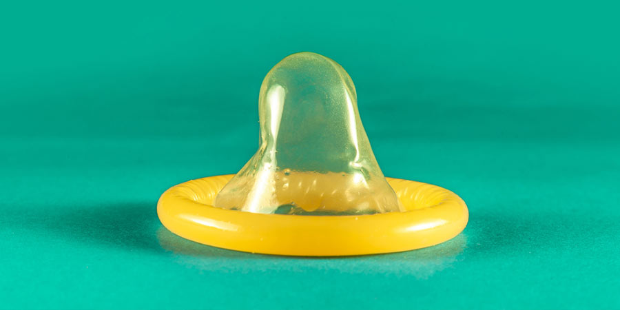 Yellow, unwrapped condom displayed on a green surface