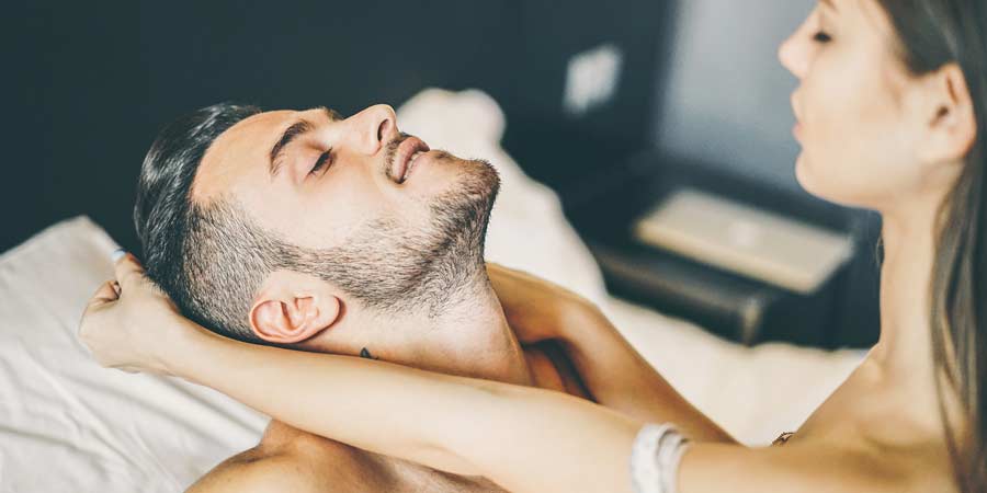 Woman dominating her partner in bed by pulling his hair roughly as they stare into each other's eyes