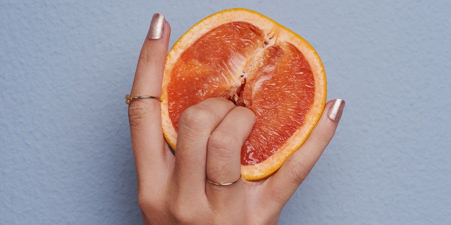 Woman's hand with two fingers pushed deeply into an orange which has been cut in half 