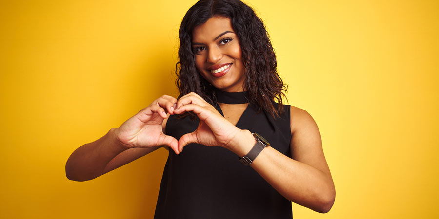 Beautiful dark skinned trans woman wearing a black dress and making a heart shape with her hands