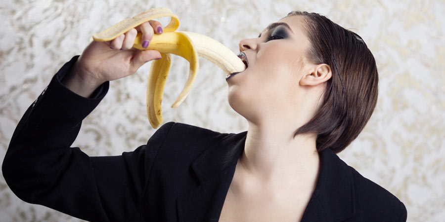 Woman leaning her head back whilst she eats a banana suggestively 