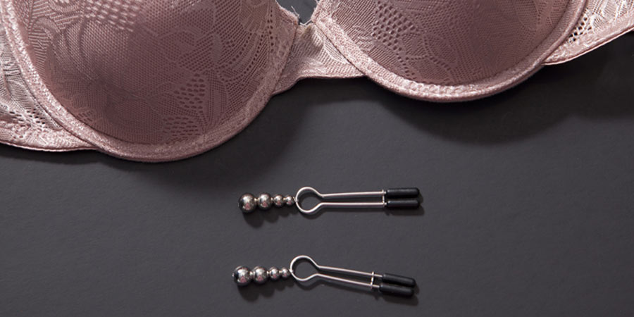 Pair of metal nipple clamps beside a pink lacy bra