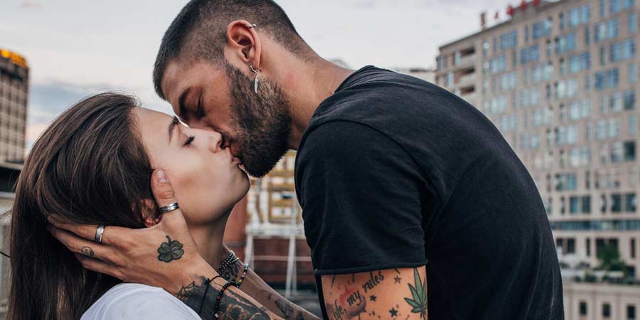 Sexy man with sleeves tattooes holding his partner's face while he passionately kisses her 