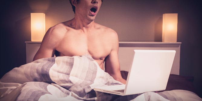 Man in bed watching porn and masturbating
