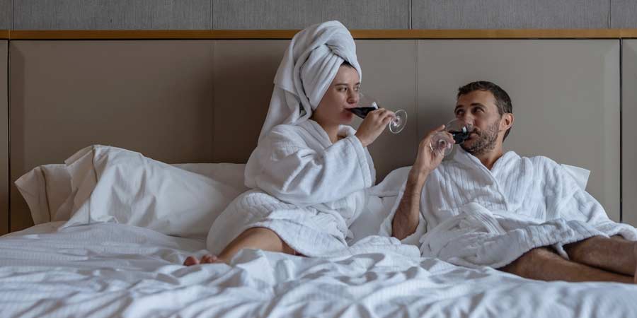 Couple sitting in bed after a shower sharing a bottle of red wine 